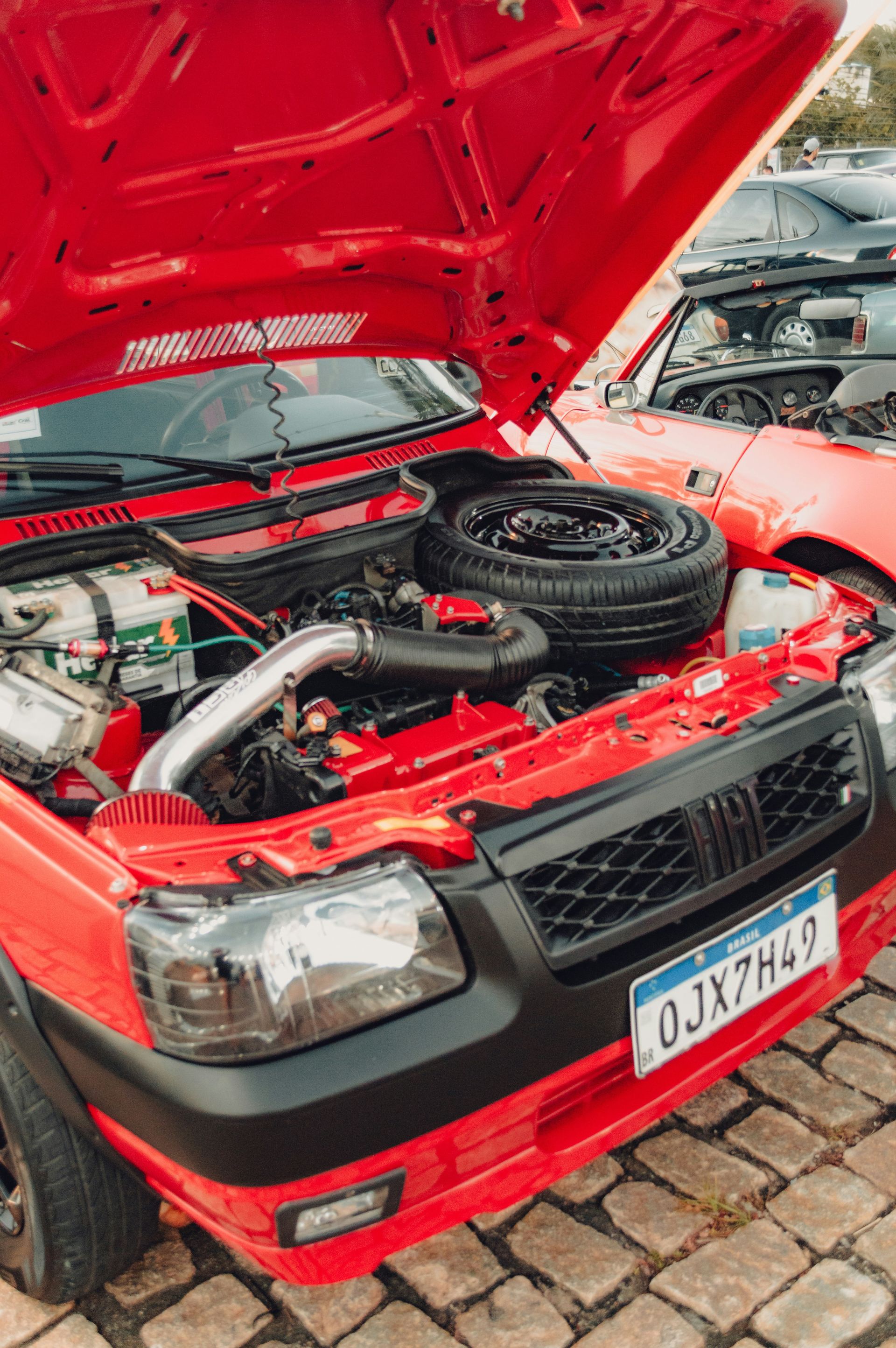 A red Fiat car with an open hood revealing the engine and spare tire